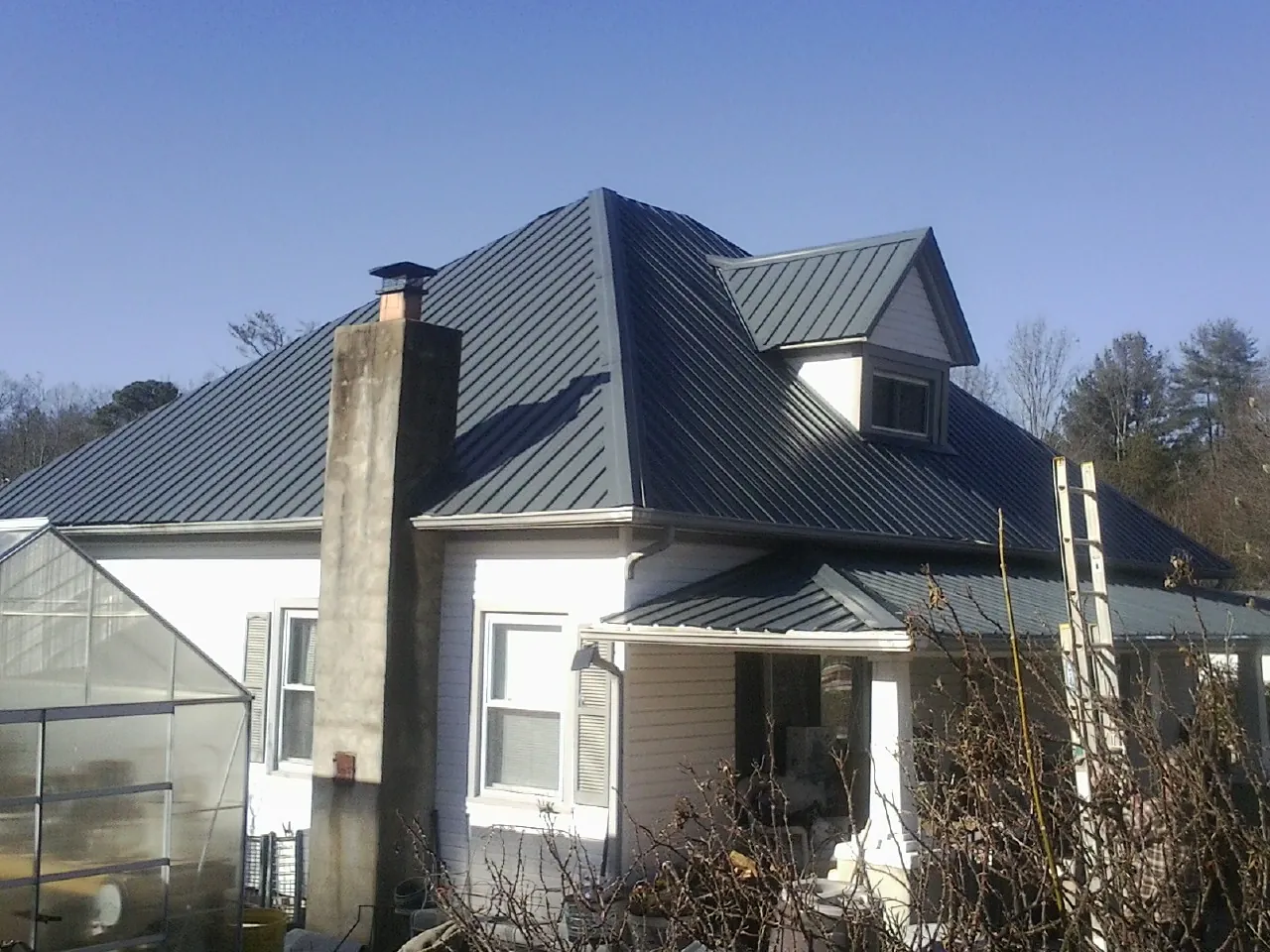 Dark blue standing seam metal roof on a white farmhouse with dormer — Slate & Tile Roof Repair by Roofing Brothers in Grayling