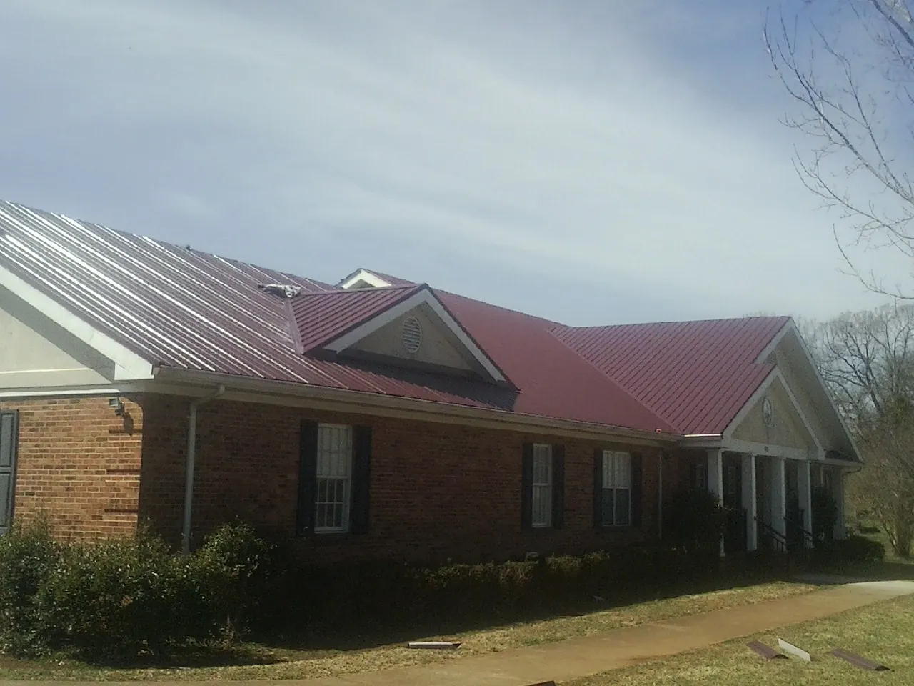 Red metal roof with gabled entries on a long brick building, from a Hail Damage Roof Repair job in Grayling