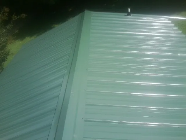 New green metal panels meeting at the ridge of a roof — Flat Roof Repair work by our crew in Grayling