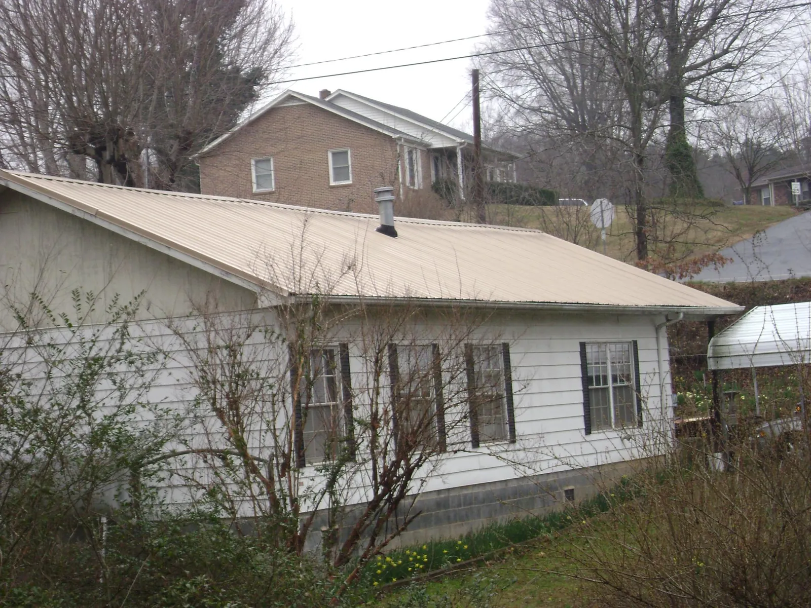 Tan metal roof on a white sided house set into a hillside — Commercial Roofing by Roofing Brothers in Grayling
