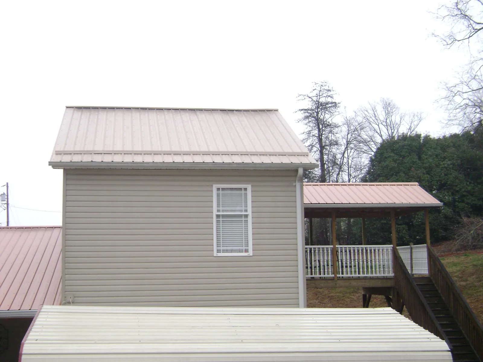 Tan metal roofs on a two story addition and attached porch, from a Roof Replacement job in Grayling