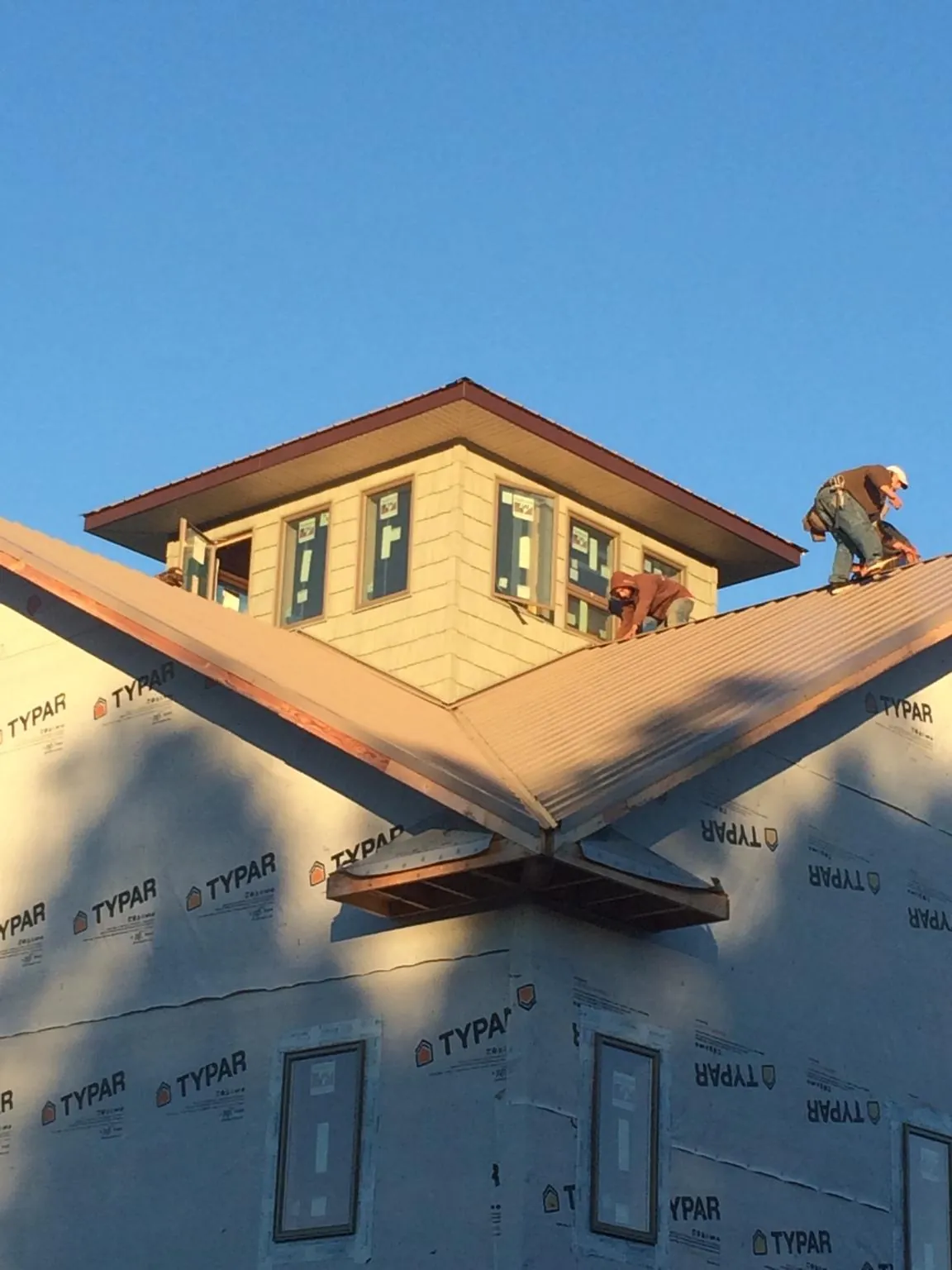 Roofers working around a rooftop cupola on a new metal roof at sunset — Roof Waterproofing in Grayling by Roofing Brothers